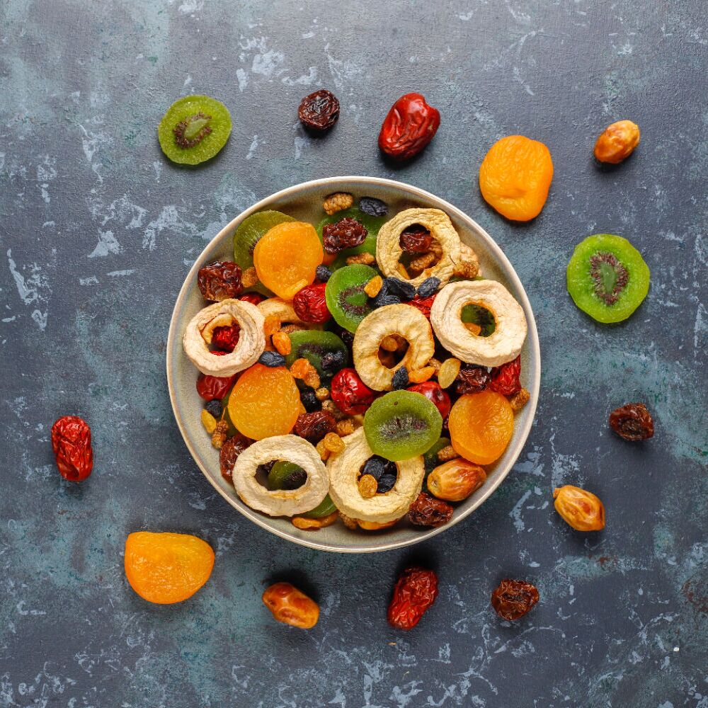  Assorted gourmet dried fruit mix in a bowl with kiwi, apple rings, apricots, and dates – vibrant healthy snack and natural energy boost.